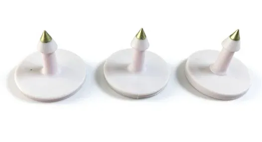 Three white ear tag pin components with round bases and gold-colored pointed tips