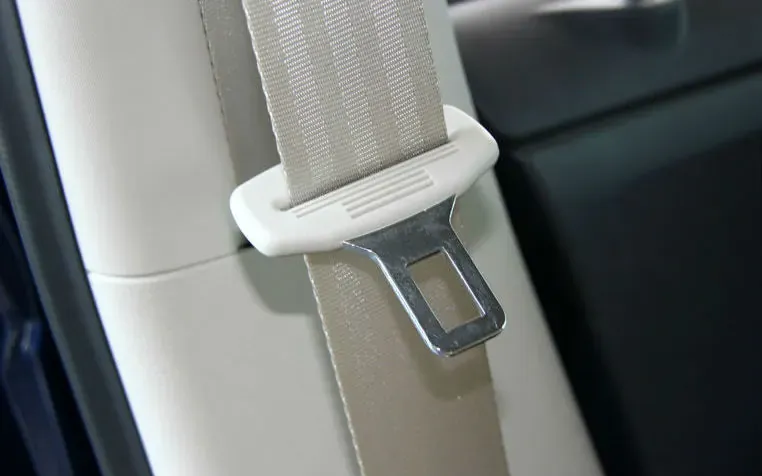 Seat belt tongue on webbing, showing its white plastic surround and projecting metal latch plate
