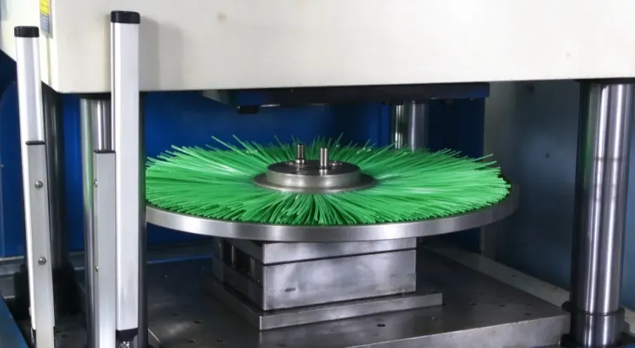 Green snow sweeper wafer brush assembly positioned in the open mold of a vertical injection molding machine